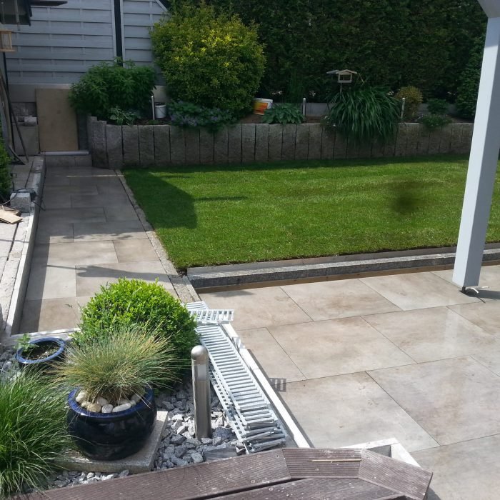 Gepflegte Rasenfläche mit Randbeet und heller Terrasse