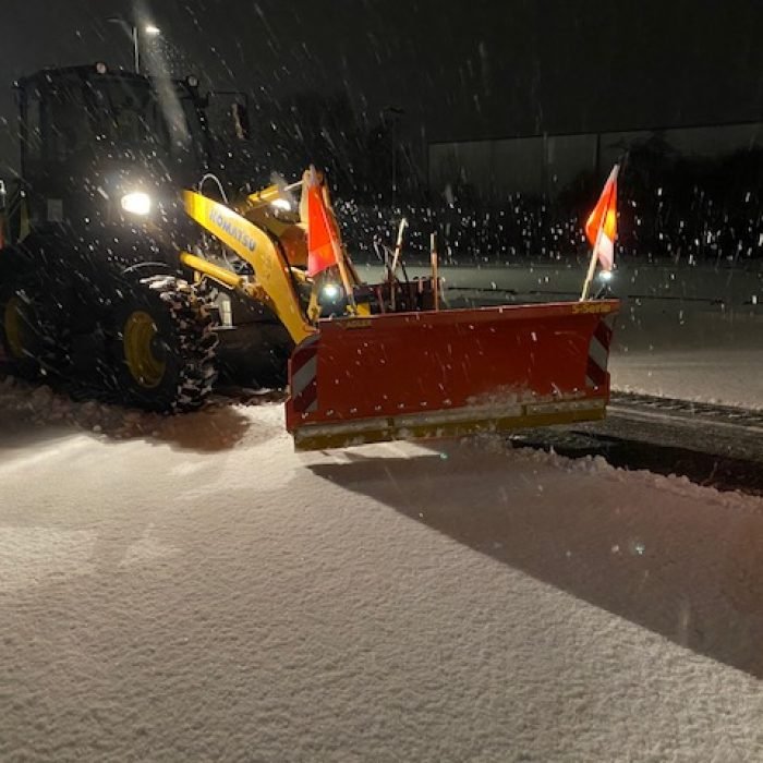 Räumfahrzeug mit Schneeschild bei nächtlichem Schneefall